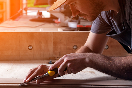 Close up of young  man builder wearing in a plaid shirt   treating a wooden product with a chisel in the workshop, close-upの写真素材