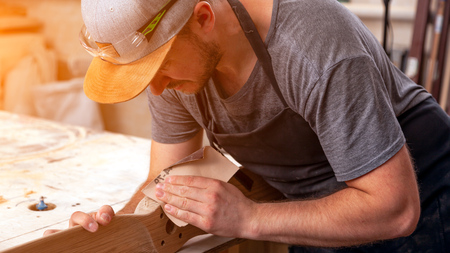 Experienced carpenter in work clothes and small buiness owner working in woodwork workshop,  using sandpaper for polishing children's helicopter blades at worktable in workshopの写真素材