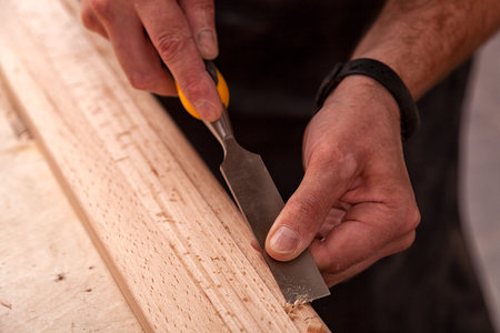 A young brunette man builder wearing green protective goggles, a gray T-shirt and a beard treating a...