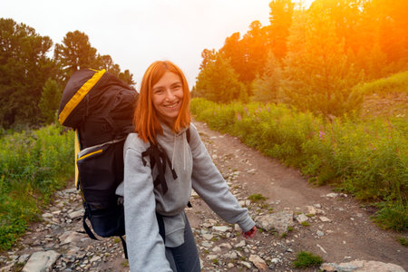 Hiking woman with backpack  cheerfully smiles, enjoys a hike in the mountains.Hipster traveler on top of forest, amazing view. Wanderlust fun and travel conceptの写真素材