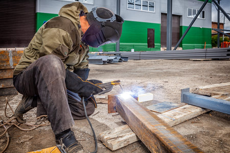 A young  man welder in brown uniform, welding mask and welders leathers, weld  metal  with a arc...