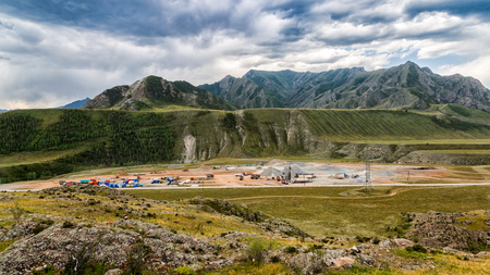 Panoramic view of large-scale construction of an industrial facility in the mountains with the help of cranes, trucks and other special equipment against the blue skyの写真素材