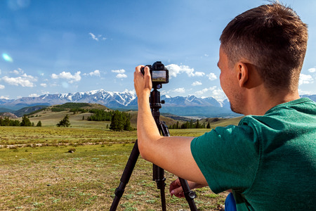 Travel photographer taking nature photo of mountain landscape. Hiker tourist professional man on adventure vacation shooting slr camera on tripod.の写真素材