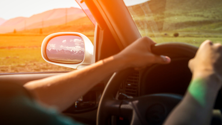driving car on the mountain road. Guy inside the car driving on the country roadway between fields with brown grass and snowy mountains . Sun is shining. Shoot from the back.の写真素材
