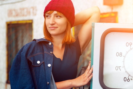 Outdoor atmospheric lifestyle photo of young beautiful  red-haired woman  in knitting hat in sunny autumn day  at the old gas station.  portrait of joyful womanの写真素材
