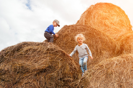 Little boy and girl on  haystacks d in the sunlight running, playing enjoying nature. Kid Raising over field and sunset sky background. Children  environment conceptの写真素材