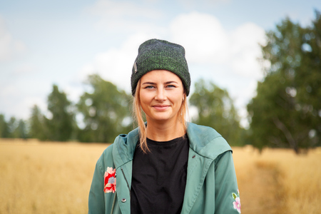 Young woman in green coat, knitting hat, jeans walking, enjoying nature and sunlight in straw field. Concept of autumn  holidays at village  and live styleの写真素材