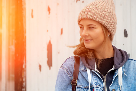 Portrait young woman in blue jeans coat, knitting hat, jeans against the background of the old lighthouse . Concept of autumn  holidays at village  and live styleの写真素材