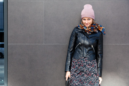 Portrait joyful young woman with  brunette hair in knitting hat, leather coat and dress having fun, smile and enjoy day on street big city. stylish hipster womanの写真素材