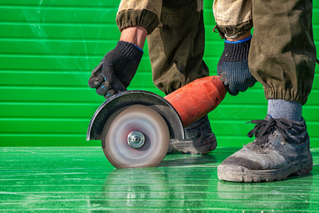 A young man welder in a working overall and working gloves grinds a metal object with a angle  grinder in the constraction sideの写真素材