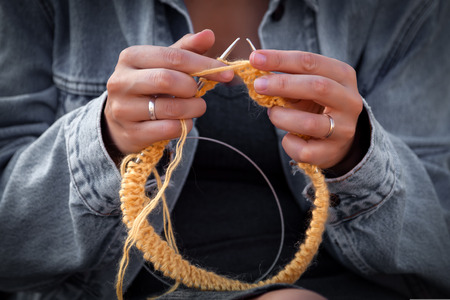 A young woman in a jeans jacket and  knitting hat with needle and natural wool on the back of the background is the autumn landscape of the field.の写真素材
