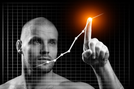 Young businessman in business concept with a graph. Young sporty man shows with his index finger a growth point on a chart on a black isolated background.の写真素材