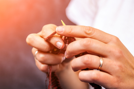 Close-up of an young woman  in white t-shirt and jeans, knits a natural wool  brown hat with knitting needles.の写真素材