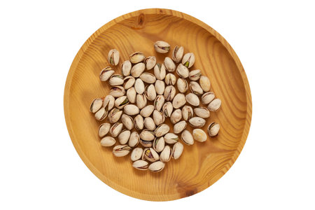 Unpeeled pistachios in a wooden pine plate on a white isolated background. Row of bowls with...