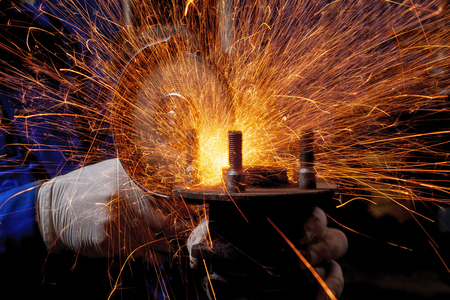 A close-up of cutting  a metal car part with a  angle grinder machine on a metal table at the factory, multi-yellow and blue sparks fly apartの写真素材