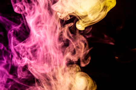 Abstract art colored pink and yellow  smoke on black isolated background. Stop the movement of multicolored smoke on dark backgroundの写真素材