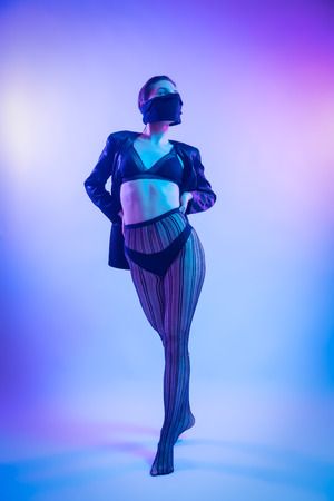 Fashion portrait of young elegant girl in in fishnet tights and underwear . Colored background, studio shot. Beautiful brunette woman posing. hipster girl in neon.の写真素材