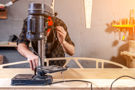 Close up of a man with work clothes and a carpenter's cap is carving a wooden board on an modern large drilling machine in a light workshop. Home repair conceptsの写真素材