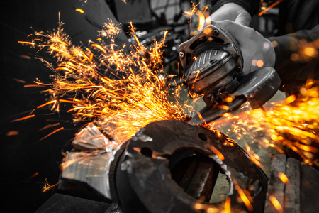 A close-up of a car mechanic using a metal grinder to cut a brake disk  in an auto repair shop, bright flashes flying in different directions, in the background tools for an auto repairの写真素材