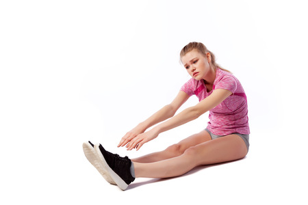 Young woman in sports clothes smilling, possing and stretching on the floor on white isolated background. Side view.Fit girl living an active lifestyleの写真素材