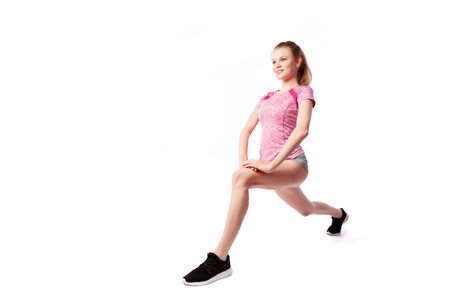 A young  woman coach in a sporty  short top and gym leggings makes lunges  by the feet forward,...