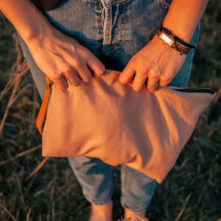 Close-up of a young woman holding a handmade bag with accessories for knitting: knitting needles, crochet hooks, pink ball of yarn, against a background of a fieldの写真素材