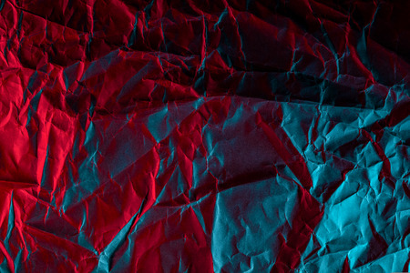 Texture of crumpled black paper. Close up black background of crumpled cardboard under color red and blue studio lightの写真素材