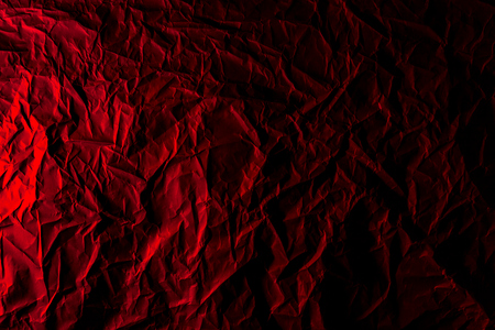 Texture of crumpled black paper. Close up black background of crumpled cardboard under red studio lightの写真素材