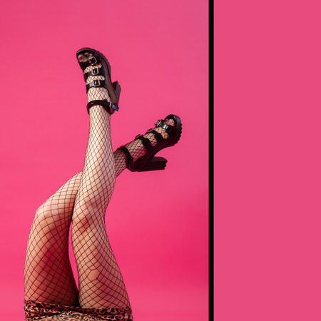 Concept of merry summer mood, relaxation and beauty. Female legs in black heels and black pantyhose in mesh on an isolated bright pink, yellow, green backgroundの写真素材