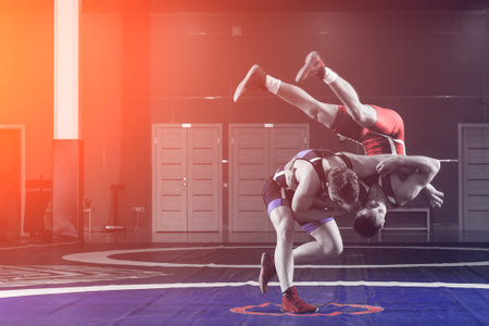 Two young men in blue and red wrestling tights are wrestlng and making a hip throw on a yellow wrestling carpet in the gym. The concept of fair wrestlingの写真素材