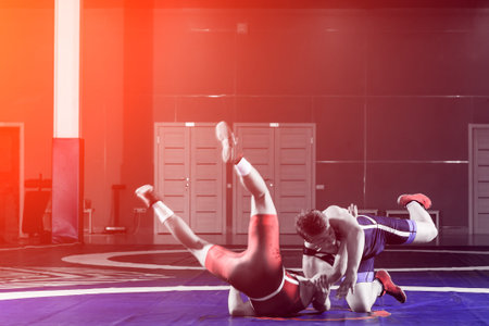 Two strong wrestlers in blue and red wrestling tights are wrestlng and making a  making a hip throw ...