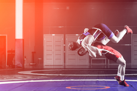 Two young men in blue and red wrestling tights are wrestlng and making a suplex wrestling on a yellow wrestling carpet in the gym. The concept of fair wrestlingの写真素材