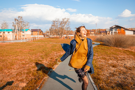 A beautiful woman in a warm sweatshirt, dress, jacket and sneakers walks, has fun, behaves funny, rests, enjoys nature on a warm summer dayの写真素材