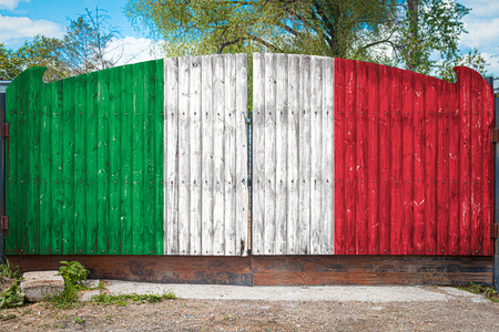 Close-up of the national flag of Italy on a wooden gate at the entrance to the closed territory on a summer day. The concept of storage of goods, entry to a closed area, tourism in Italyの写真素材