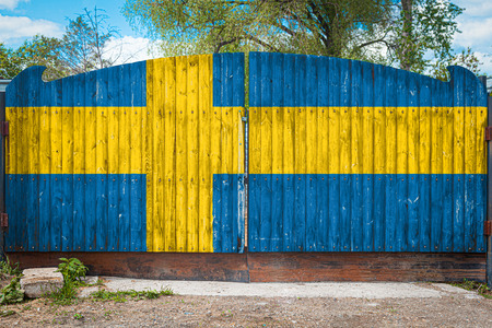 Close-up of the national flag of Sweden on a wooden gate at the entrance to the closed territory on a summer day. The concept of storage of goods, entry to a closed area, tourism in Swedenの写真素材