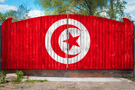 Close-up of the national flag of Tunisia on a wooden gate at the entrance to the closed territory on a summer day. The concept of storage of goods, entry to a closed area, tourism in Tunisiaの写真素材