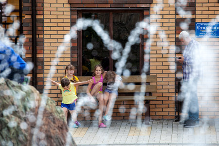 Altai, Russia â August 08, 2018:  a company of teenagers children sit on a bench, have fun and play in the summer international camp in the Chemalsky district, Altai Territory, view through fountain dropsのeditorial素材