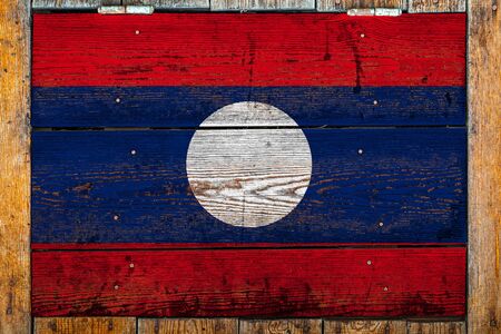 National flag of Laos on a wooden wall background.The concept of national pride and symbol of the country.Flag painted on a wooden fence with metal nails.の写真素材