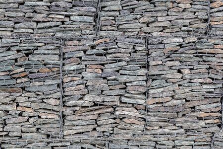 A wall lined with small gray stones behind a metal grate so that the mountains do not crumble. Stone textureの写真素材