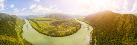 Panoramic view on mountain river, small village in front of mountain range.  National park in Altai...