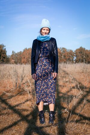 Portrait female student on field background. Beautiful modern  young woman wearing gray knitting hat  and  coat smile, look at the camera and enjoy autumn sunny day.の写真素材