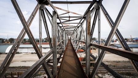 The metal bridge of their structures against the background of a construction site, in the background industrial warehouses for storing goods.Large metal gantry cranes at a construction site against the blue sky.の写真素材