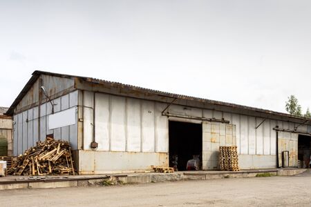 A large metal industrial warehouse for storing goods, next to it are wooden pallets for storing goods. Industrial concept of transportation, loading and storage of goodsの写真素材
