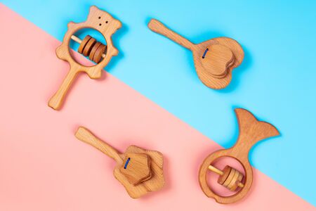 Multi-colored flat lay with eco-friendly wooden toys, rattles in the form of a heart, fish, stars, bear on pink and blue isolated background.  Top view, template for kids learning and entertainmentの写真素材