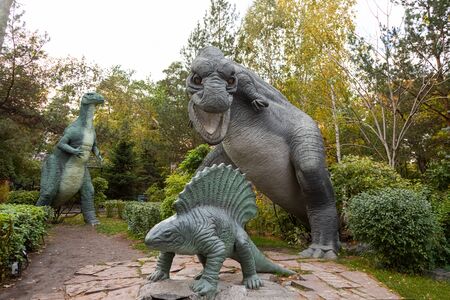 A large gray adult tyrannosaurus attacks a small stegosaurus cub near small trees and shrubs on a warm autumn day. Dinosaur worldの写真素材