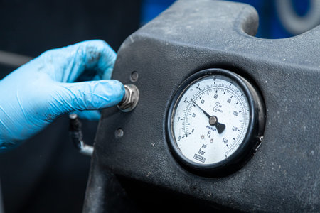Close-up A workshop worker in protective gloves presses a button on a car tire changer with a wheel...