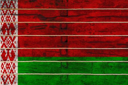 National flag  of Belarus
 on a wooden wall background. The concept of national pride and a symbol of the country. Flags painted on a wooden fence with a ropeの写真素材