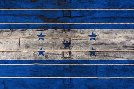 National flag  of  Honduras
on a wooden wall background. The concept of national pride and a symbol of the country. Flags painted on a wooden fence with a ropeの写真素材