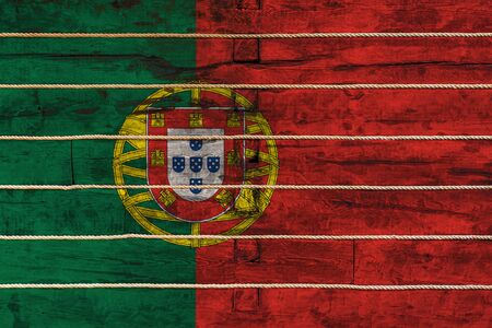 National flag  of Portugal on a wooden wall background. The concept of national pride and a symbol of the country. Flags painted on a wooden fence with a ropeの写真素材