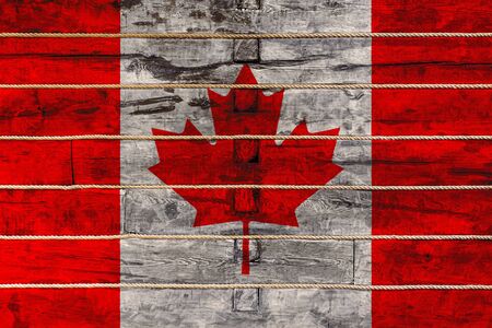 National flag  of Canada on a wooden wall background. The concept of national pride and a symbol of the country. Flags painted on a wooden fence with a ropeの写真素材
